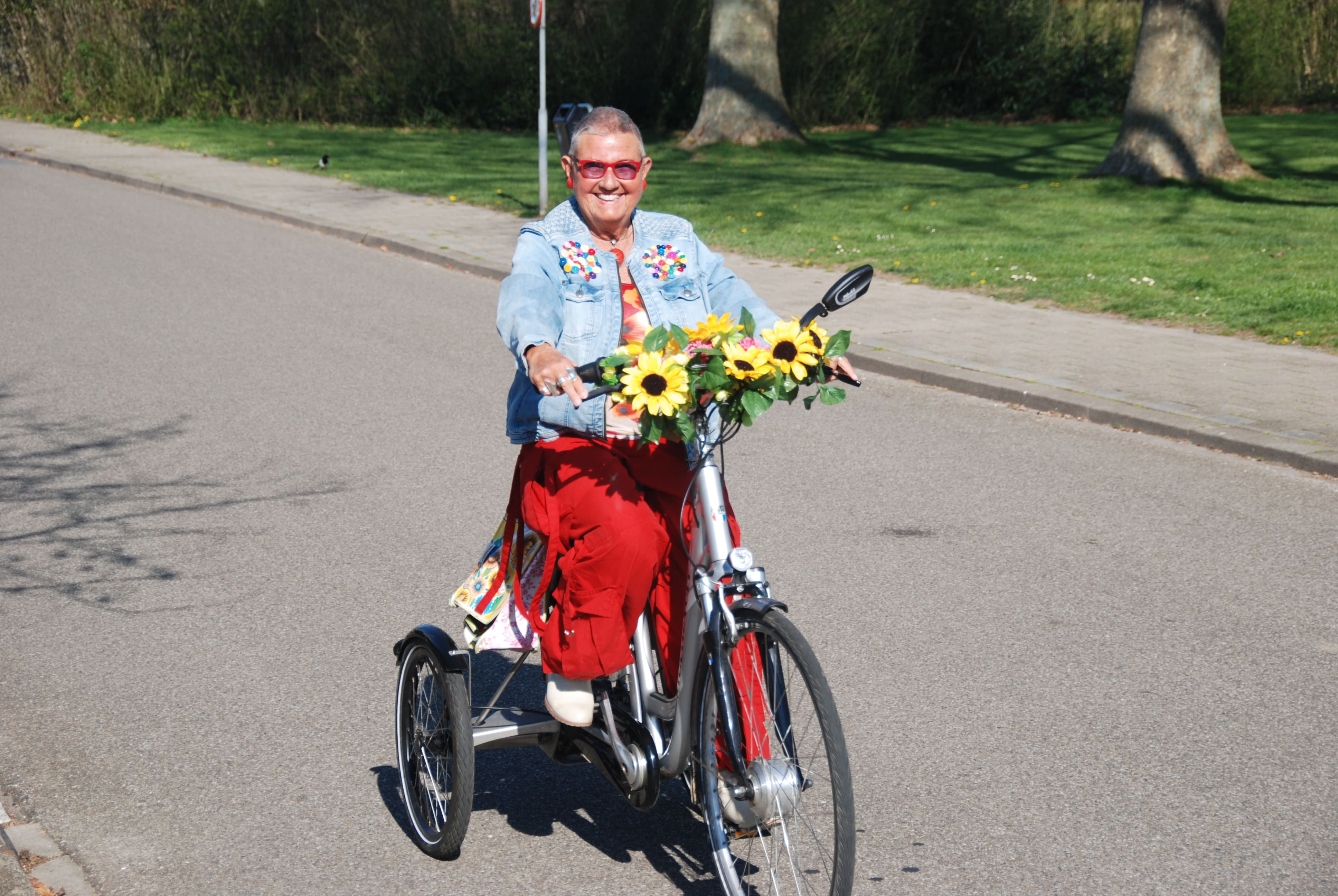 Astrid fietst op haar eigen omgebouwde driewielfiets met Tworby-module, versierd met bloemen, en lacht vrolijk.